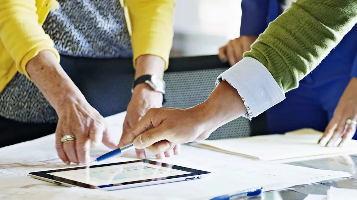 Hands of diverse professionals collaborating over plans and a tablet on a conference table, engaged in a brainstorming session.