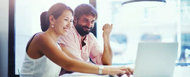 A woman and a man collaborate at a laptop in a bright, modern workspace, engaged in discussion and problem-solving.