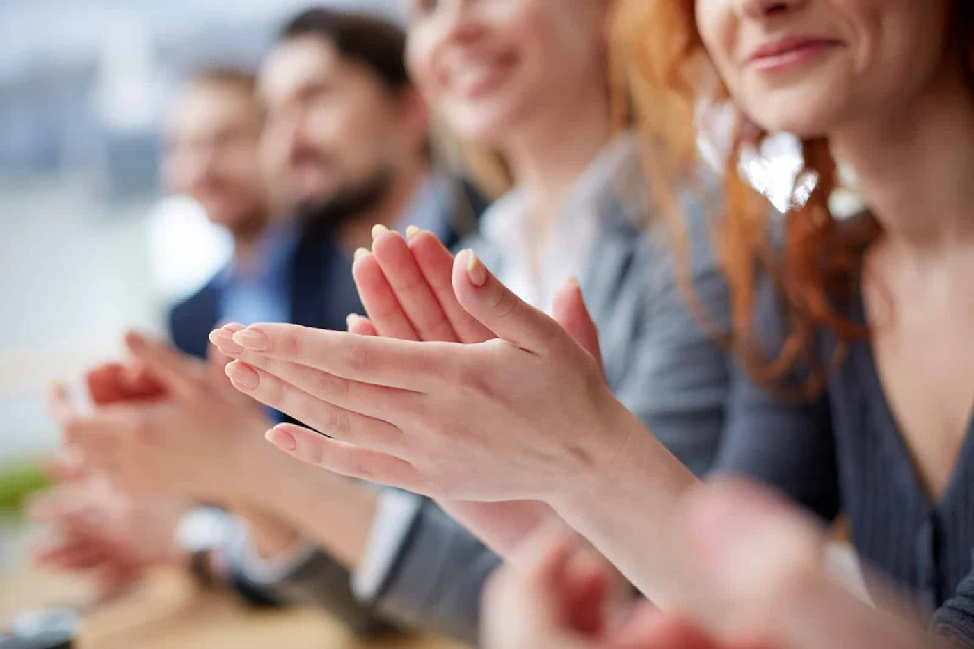 A group of people clapping in a meeting, showcasing hands in a supportive atmosphere, with blurred individuals in the background.